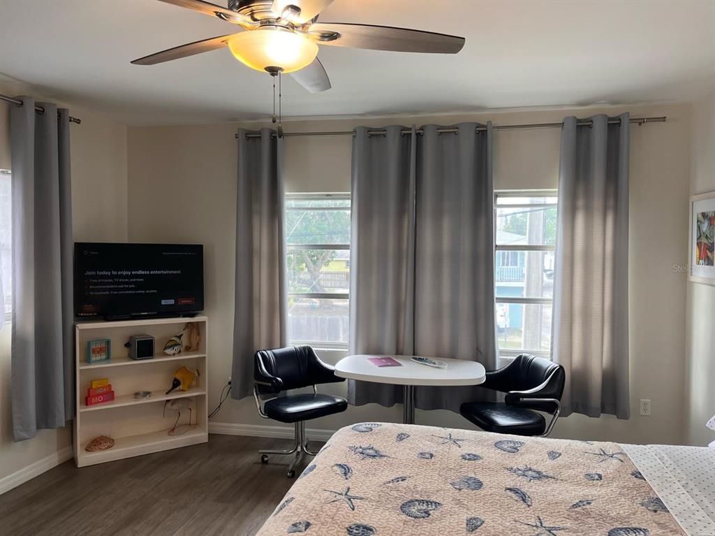 A bedroom features a ceiling fan, a television on a shelf, and a small dining table — 1901 HYDE PARK ST UNIT G, SARASOTA, FL