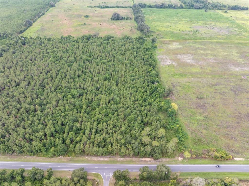 An aerial view shows a large wooded area adjacent to an open field and highway — 17198 SW STATE ROAD 47, FORT WHITE, FL