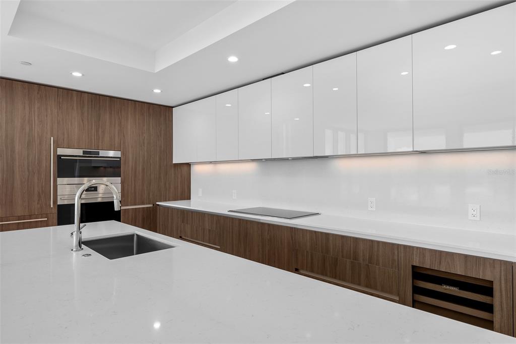 A modern kitchen features white glossy upper cabinets, wood-grain lower cabinets, and a white countertop — 5713 BOWEN DANIEL DR. UNIT 1506, TAMPA, FL
