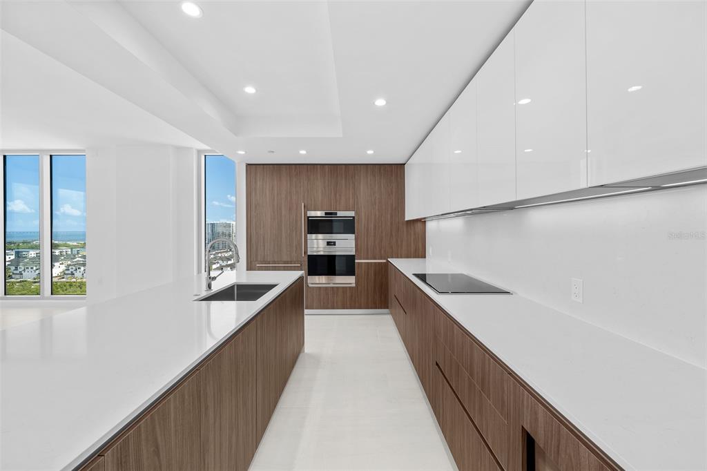 A modern kitchen features white countertops, wood-toned cabinetry, and floor-to-ceiling windows with a water view — 5713 BOWEN DANIEL DR. UNIT 1506, TAMPA, FL