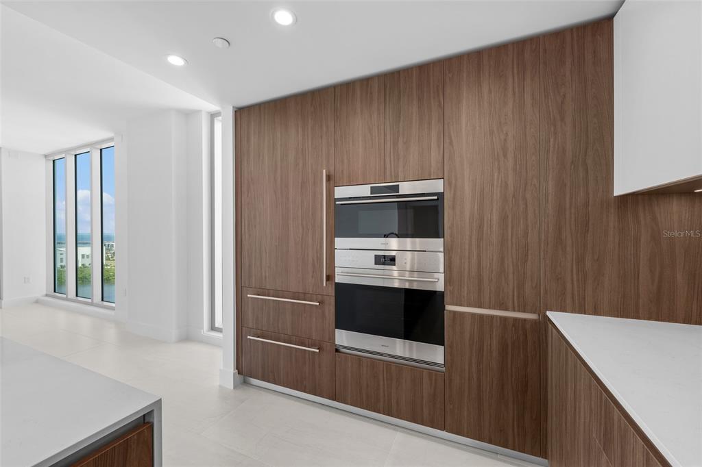 A modern kitchen features wood-grain cabinetry, stainless steel wall ovens, and white countertops — 5713 BOWEN DANIEL DR. UNIT 1506, TAMPA, FL