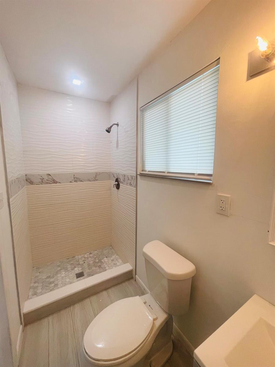 A bathroom features a walk-in shower with textured tile, a toilet, and a window — 11361 NW 32nd Place, Sunrise FL 33323, SUNRISE, FL