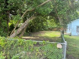 A fenced, grassy vacant lot is bordered by mature trees and a blue house — 2901 E YUKON STREET, TAMPA, FL