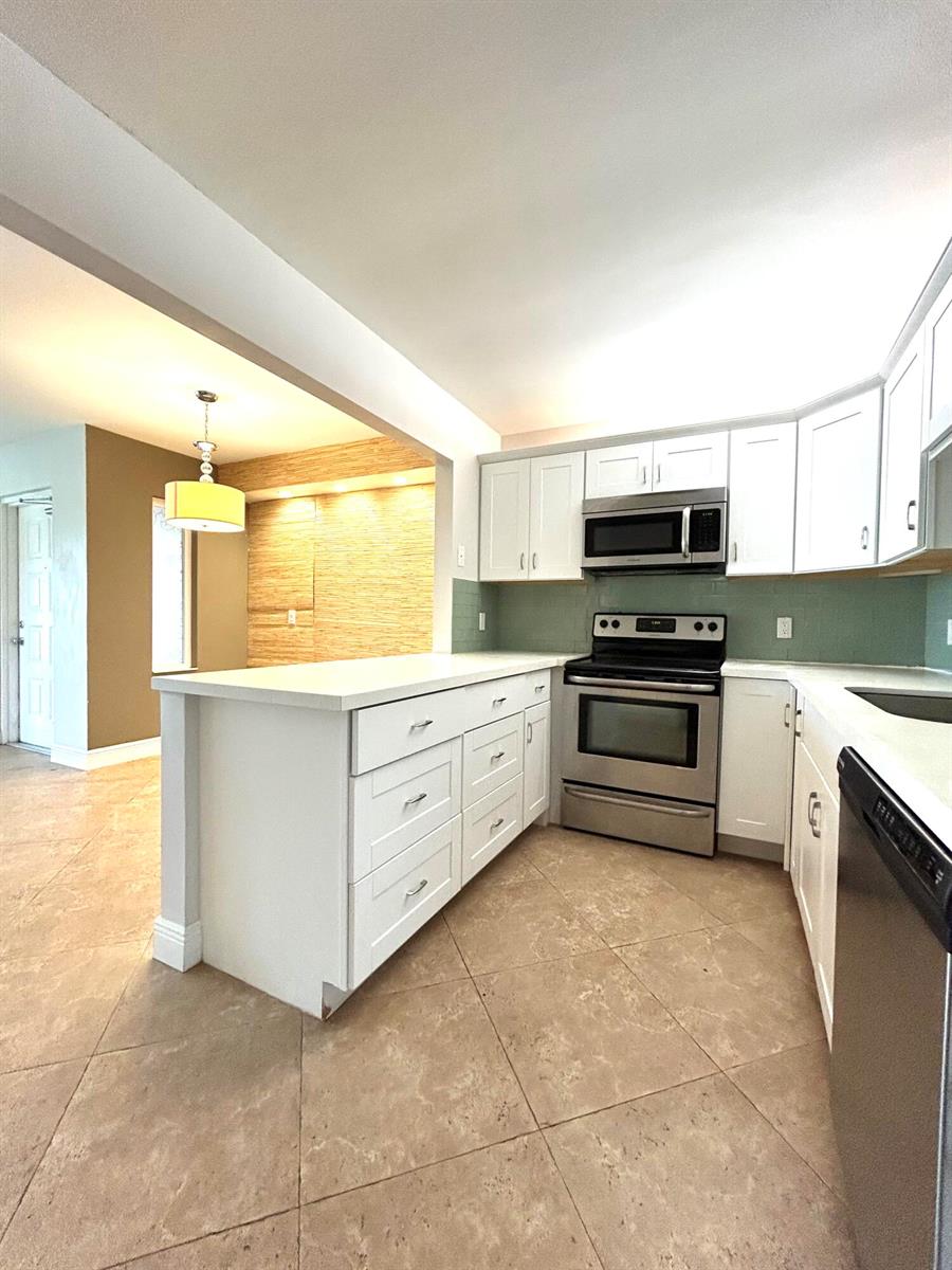 A kitchen with white cabinets, stainless steel appliances, white countertops, and a light green backsplash — 13830 Oneida Drive # G1, Delray Beach FL 33446, DELRAY BEACH, FL