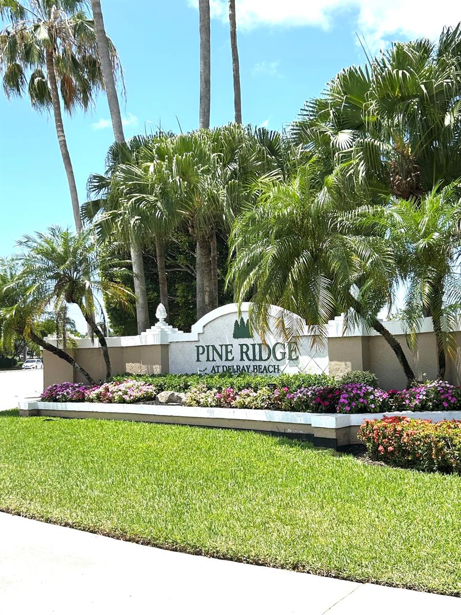 A stone monument sign for Pine Ridge at Delray Beach sits amidst palm trees — 13830 Oneida Drive # G1, Delray Beach FL 33446, DELRAY BEACH, FL