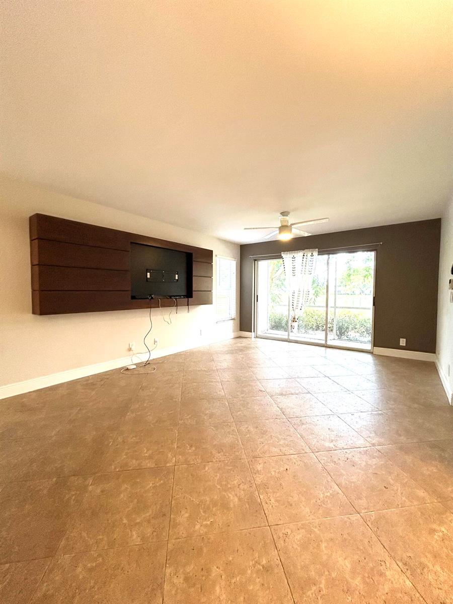 A living room features large beige floor tiles, a dark wood media wall, and sliding doors — 13830 Oneida Drive # G1, Delray Beach FL 33446, DELRAY BEACH, FL