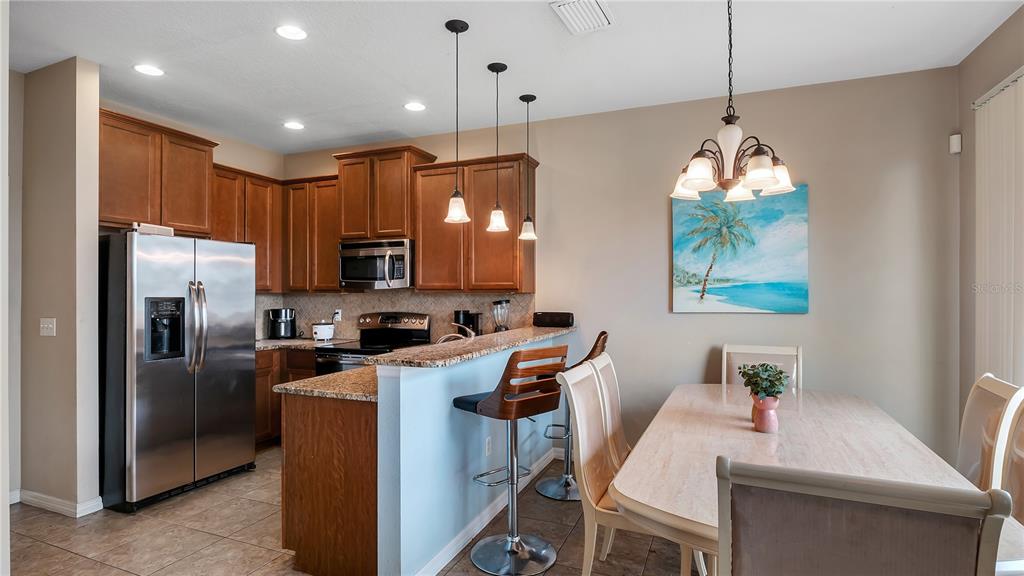A kitchen with wood cabinets and granite countertops opens to a dining area with chairs — 10235 VILLA PALAZZO COURT, TAMPA, FL