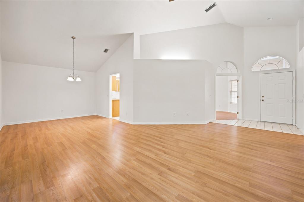 An empty room with vaulted ceilings, light wood-look flooring, and a white front door — 1034 NW 122ND TERRACE, NEWBERRY, FL