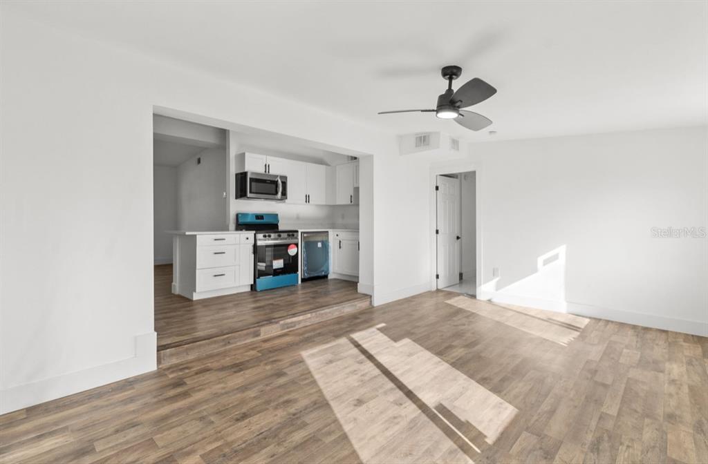 A living room with wood-look flooring leads to a raised kitchen with white cabinets — 2360 EDNOR STREET, PORT CHARLOTTE, FL