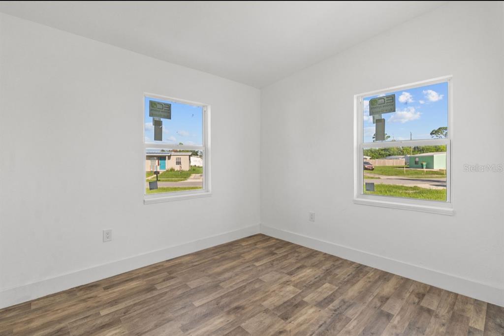 An empty bedroom features white walls, wood-look flooring, and two windows overlooking a neighborhood — 2360 EDNOR STREET, PORT CHARLOTTE, FL