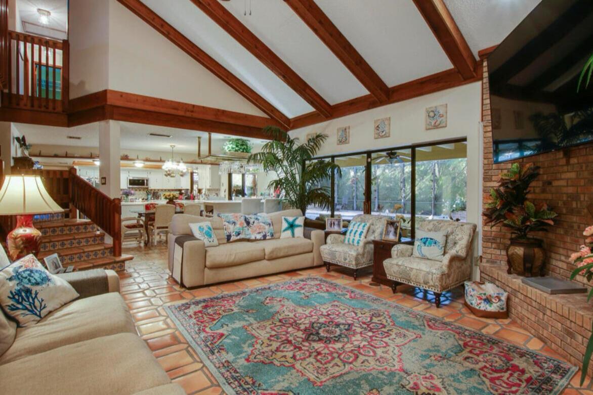 A living room with vaulted wood-beamed ceilings, tile floors, a brick fireplace, and an area rug — 12288 N 165th Rd Road N, FL 33478, FL