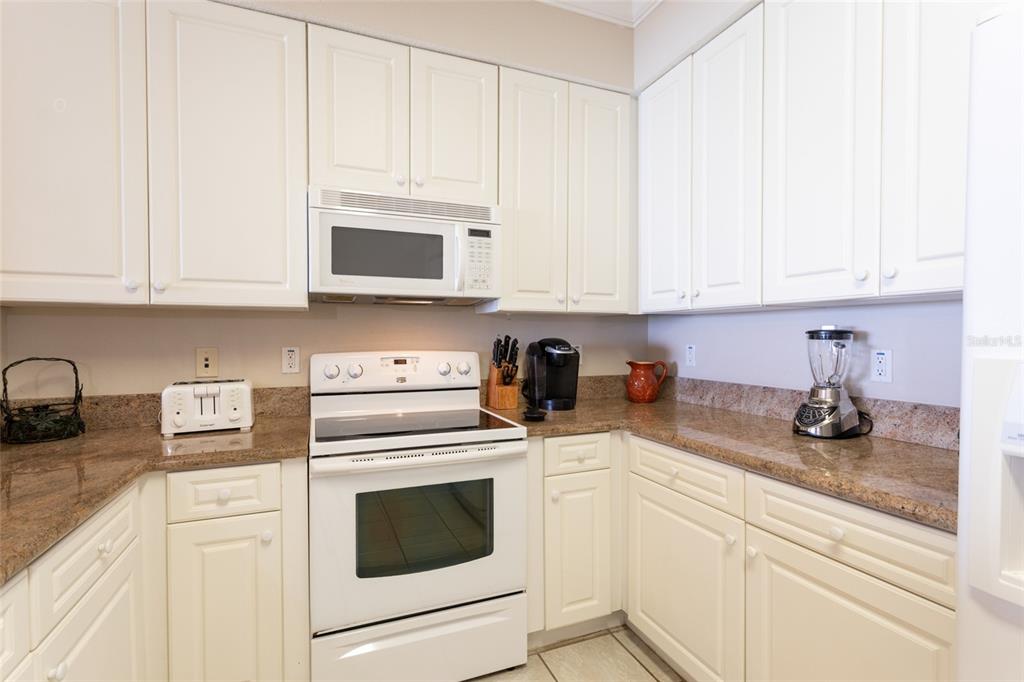 A kitchen features white cabinets, granite countertops, and white appliances — 60 SURFVIEW DRIVE UNIT 804, PALM COAST, FL