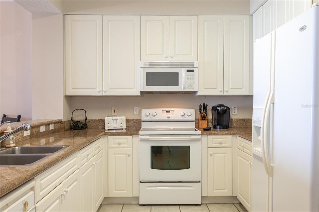 A kitchen with white cabinets, granite countertops, and white appliances including a stove and refrigerator — 60 SURFVIEW DRIVE UNIT 804, PALM COAST, FL