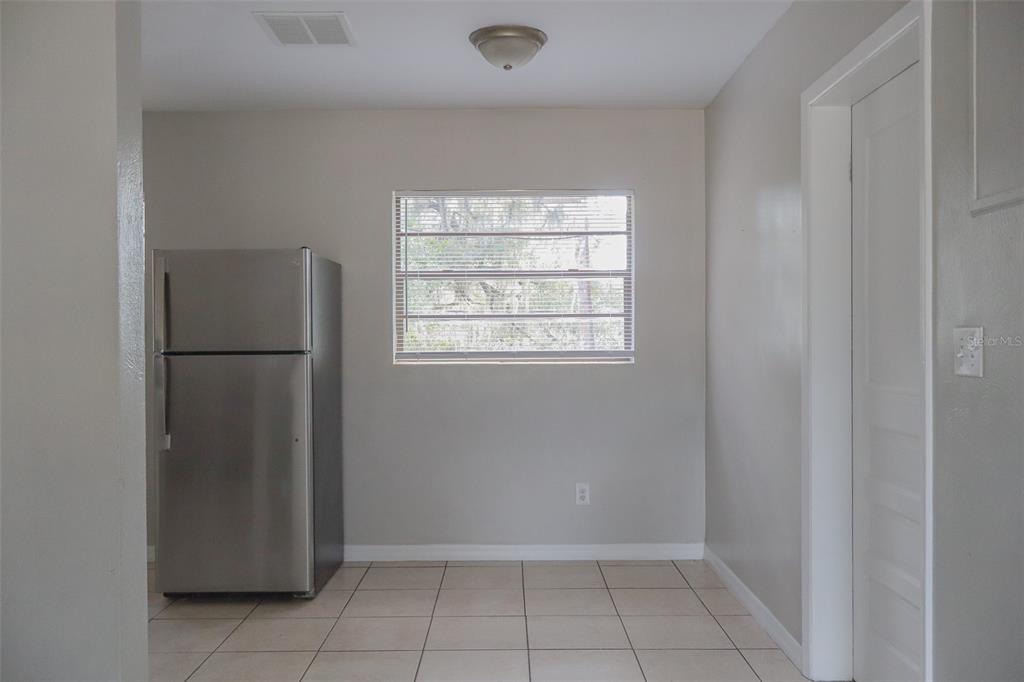A kitchen area features a stainless steel refrigerator, a window with blinds, and tiled flooring — 2708 DIXIE ROAD, LAKELAND, FL
