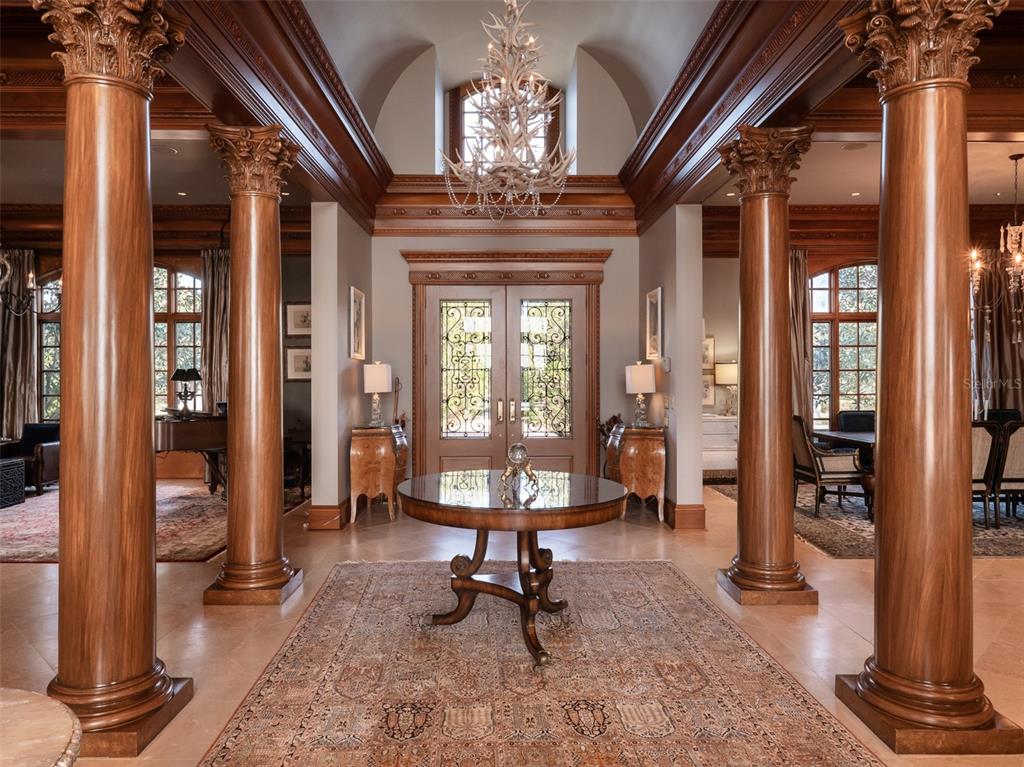 A grand foyer features tall wooden columns, a central round table, and an antler chandelier — 9001 NW 200TH STREET ROAD, MICANOPY, FL