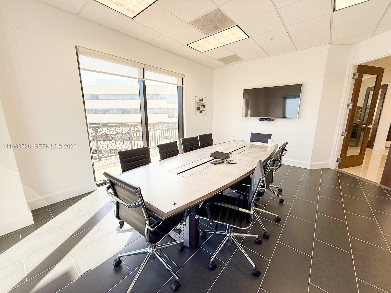 A conference room features a long table, black chairs, a wall-mounted television, and tiled flooring — 2020 Ponce De Leon Blvd, Coral Gables FL 33134, CORAL GABLES, FL