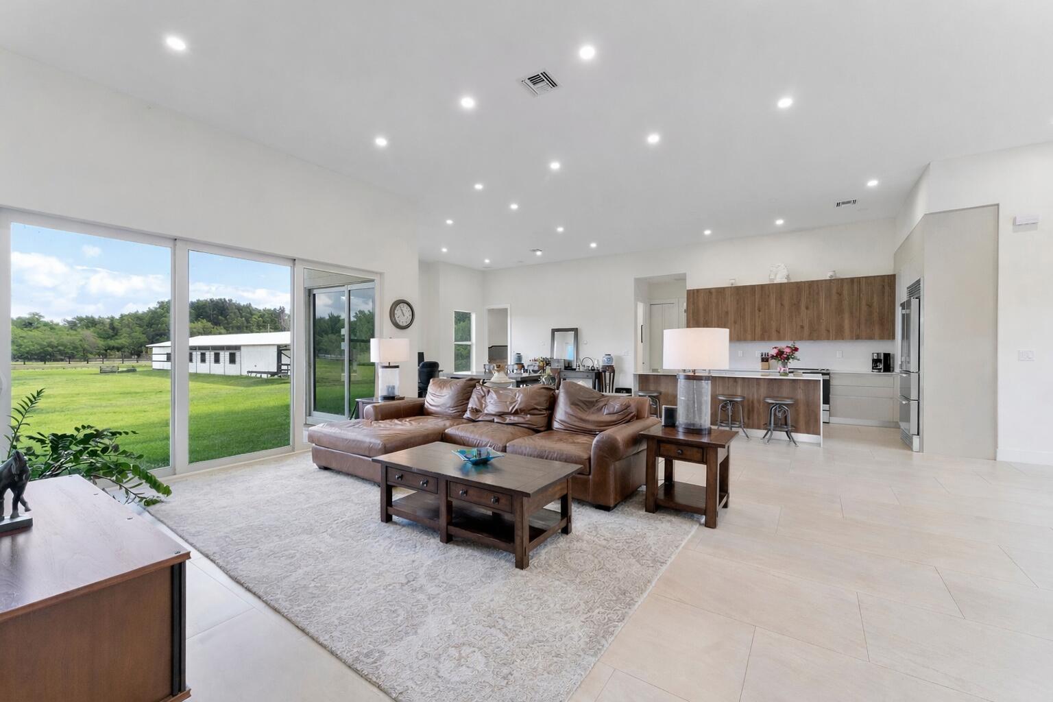 A spacious open-concept living room and kitchen with a leather sectional and large glass doors — 19921 Skyhawk Lane, FL 33470, FL