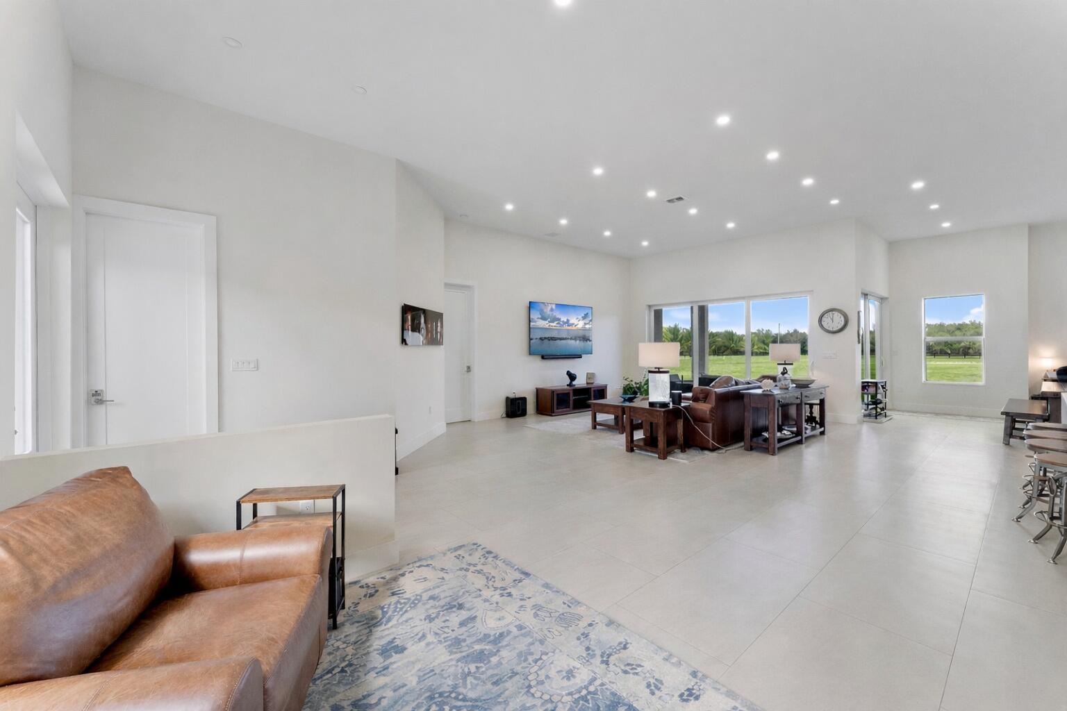 A spacious, open-concept living room with white walls, tile flooring, and large windows — 19921 Skyhawk Lane, FL 33470, FL