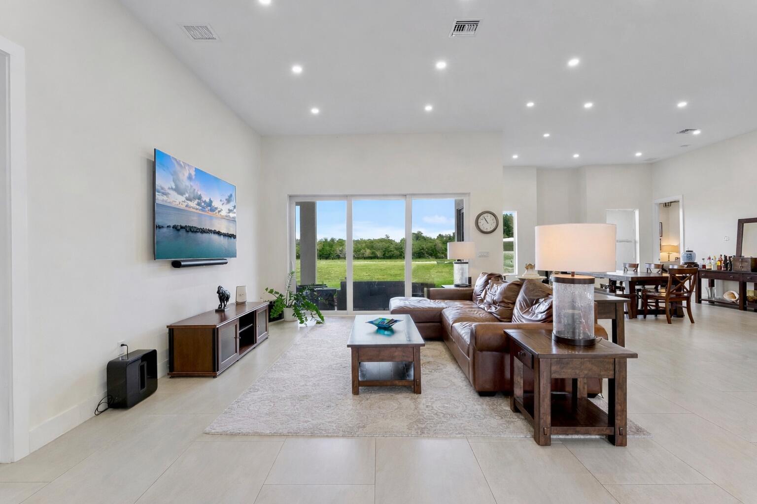 A spacious living room features a leather sectional, wooden furniture, and large sliding glass doors — 19921 Skyhawk Lane, FL 33470, FL