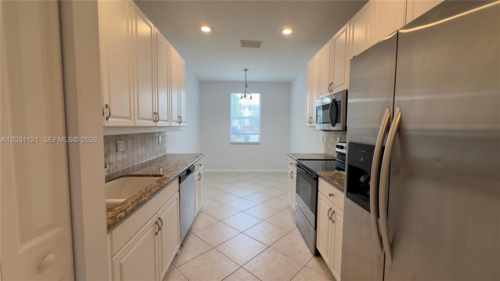 A galley kitchen features white cabinets, granite countertops, stainless steel appliances, and tile flooring — 1587 Frederick Small Rd, Jupiter FL 33458, JUPITER, FL