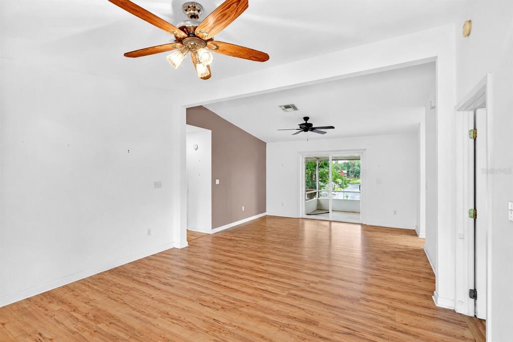 An empty living area features wood-look flooring, white walls, two ceiling fans, and sliding doors — 125 ANN STREET, HAWTHORNE, FL
