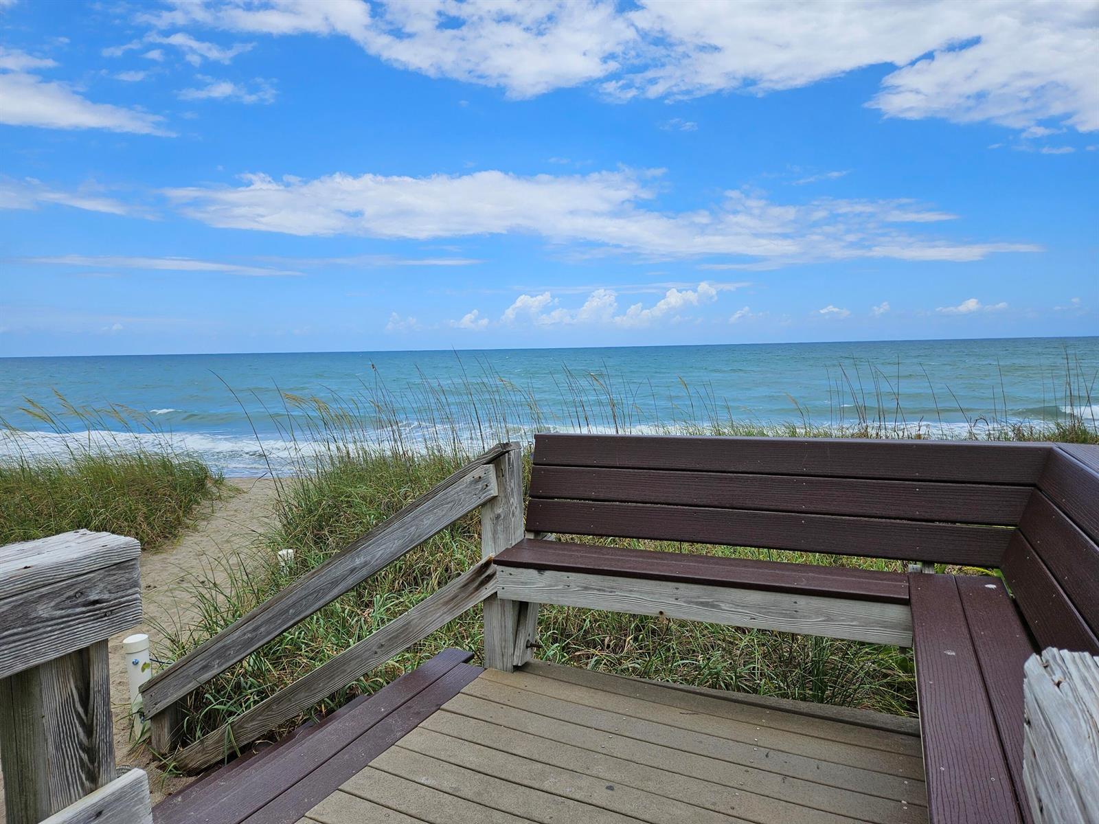 A wooden bench sits on a deck overlooking a sandy path leading to the ocean — 10701 S Ocean Drive, Jensen Beach FL 34957, JENSEN BEACH, FL