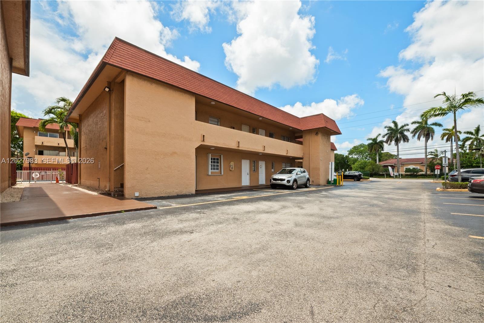 A two-story tan apartment building with a red roof stands beside a paved parking lot — 9950 SW 88th St # 4, Miami FL 33176, MIAMI, FL