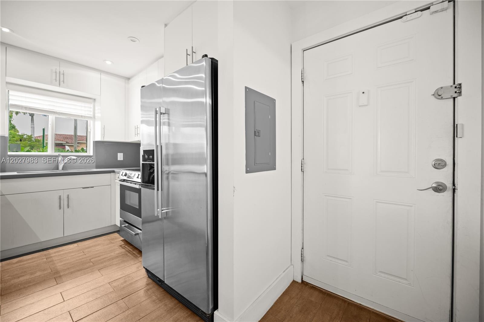 A kitchen features stainless steel appliances, white cabinetry, and wood-look flooring next to an entrance door — 9950 SW 88th St # 4, Miami FL 33176, MIAMI, FL