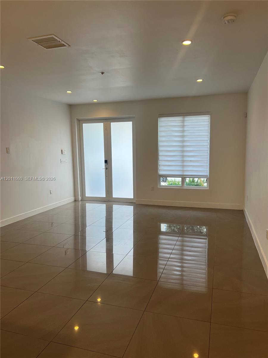 An empty room features large beige floor tiles, white walls, a glass door, and a window — 10245 NW 63rd Ter # 103, Doral FL 33178, DORAL, FL