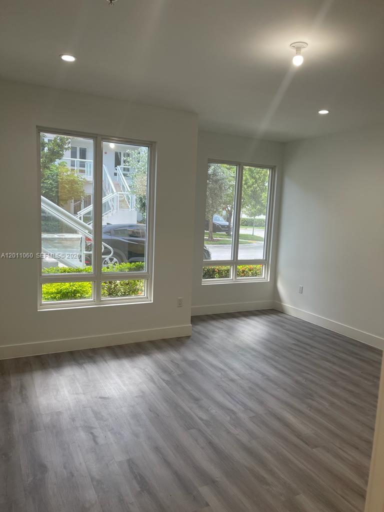 An empty room features light wood-look flooring, white walls, and large windows with exterior views — 10245 NW 63rd Ter # 103, Doral FL 33178, DORAL, FL