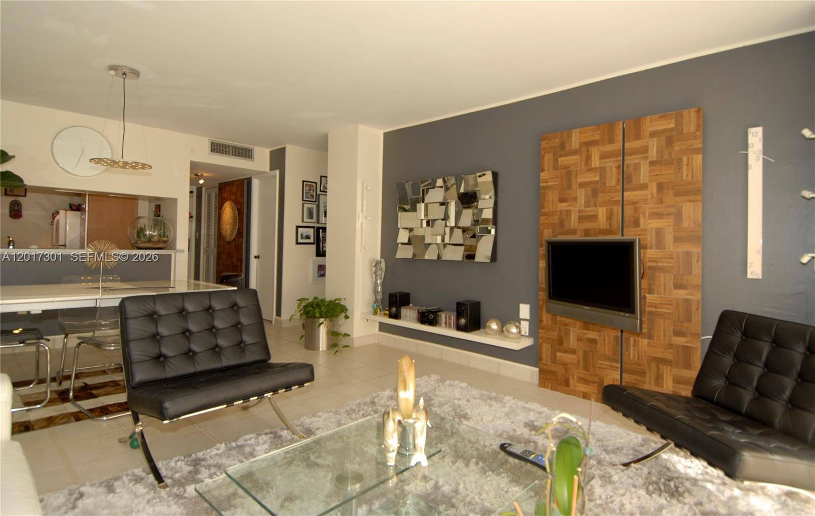 A modern living room features two black leather chairs, a glass coffee table, and a television — 600 NE 36 ST # 1212, Miami FL 33137, MIAMI, FL