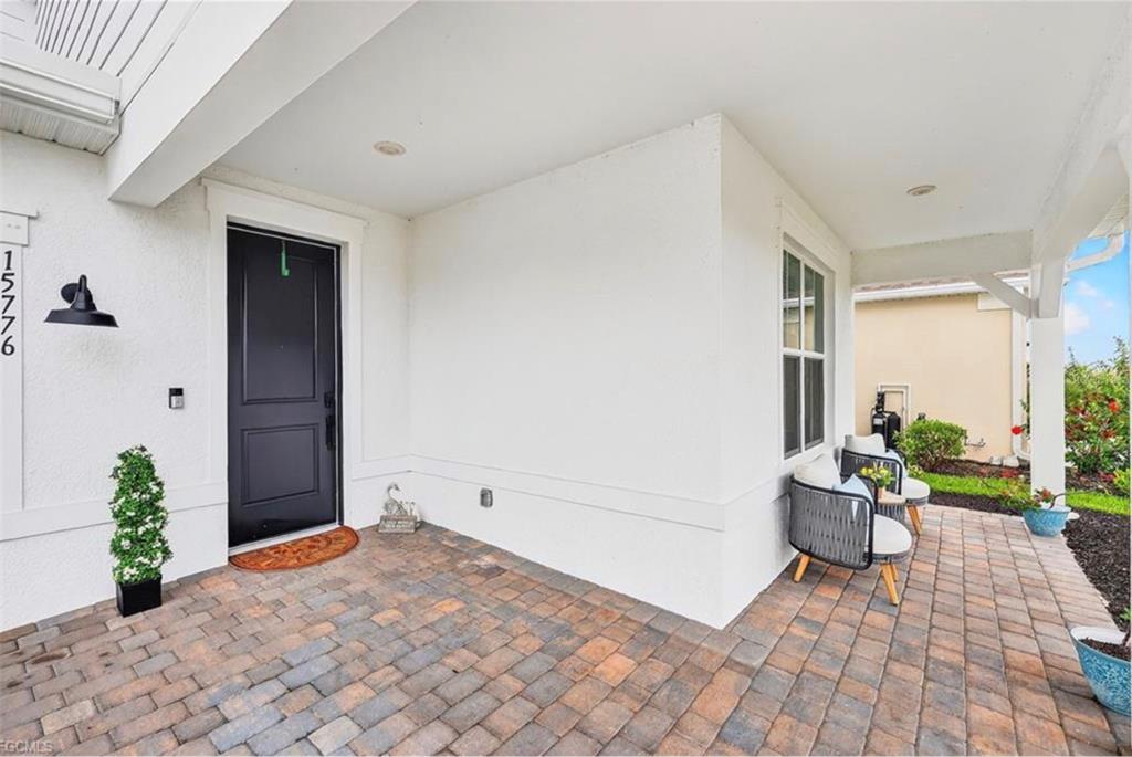 A covered front porch features a black door, paver flooring, and two outdoor chairs — 15776 APPALACHIAN DRIVE, PUNTA GORDA, FL