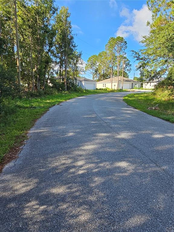 A paved road leads toward several single-story houses surrounded by trees under a blue sky — 108 SAIL WAY, POINCIANA, FL