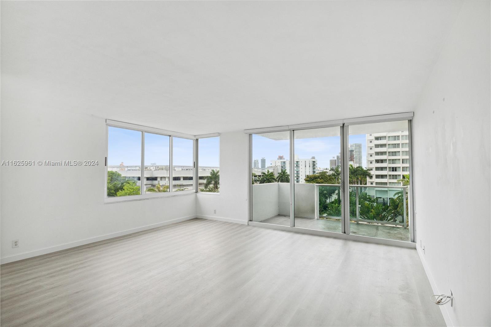 An empty room features light wood-look flooring, white walls, and floor-to-ceiling windows leading to a balcony — 1200 West Ave # 515, Miami Beach FL 33139, MIAMI BEACH, FL