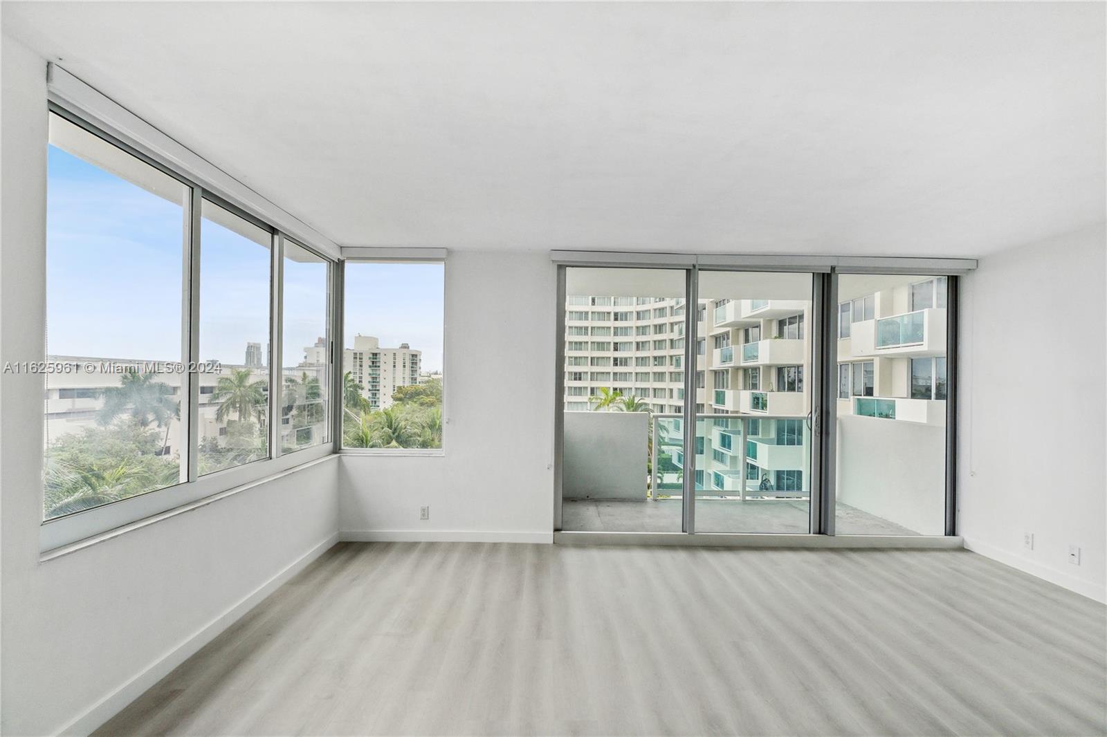 An empty room with light wood-look flooring, white walls, large windows, and a sliding glass door — 1200 West Ave # 515, Miami Beach FL 33139, MIAMI BEACH, FL