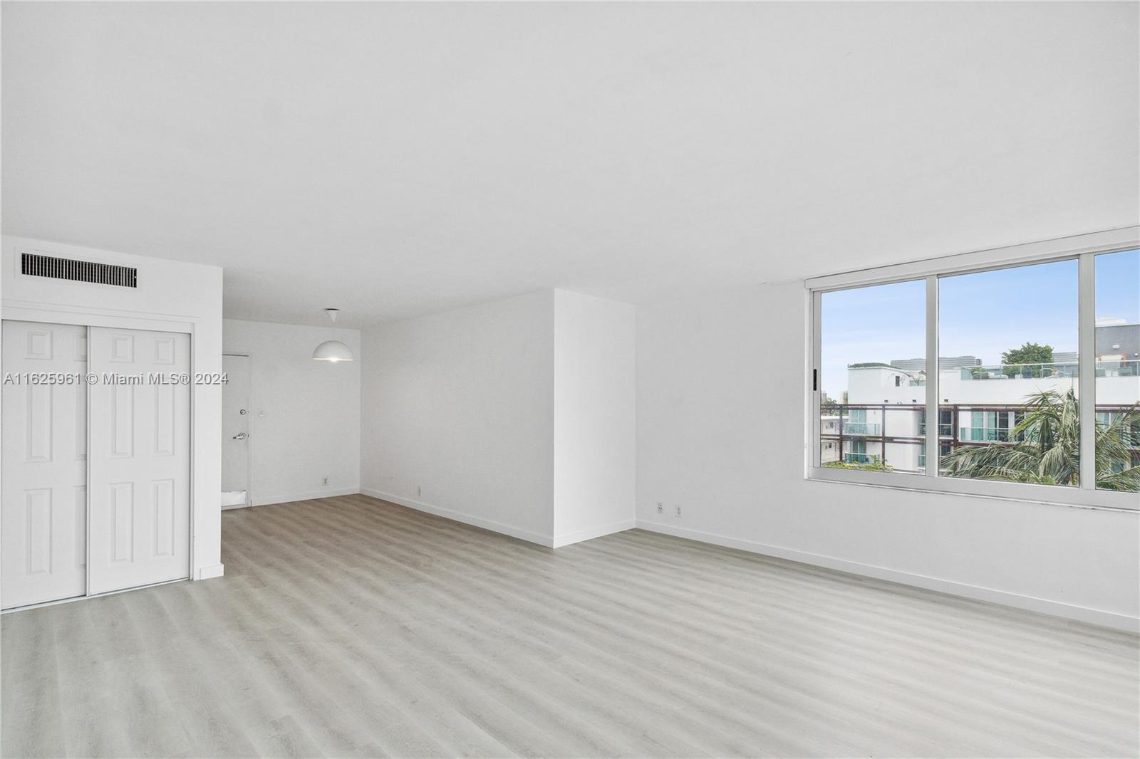 An empty room features light wood-look flooring, white walls, a sliding closet, and large windows — 1200 West Ave # 515, Miami Beach FL 33139, MIAMI BEACH, FL
