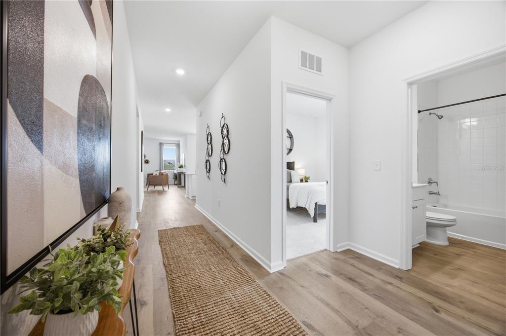 A hallway with light wood floors leads to a bedroom and a bathroom with a tub — 5731 HIAWASSEE ROAD, OKAHUMPKA, FL