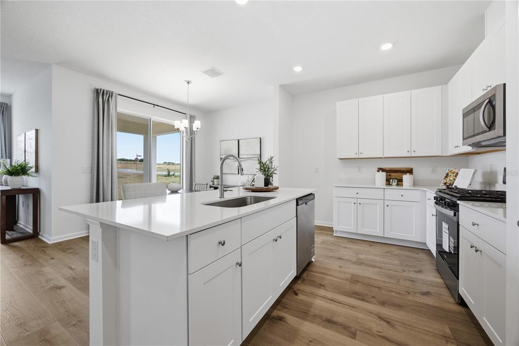A modern kitchen features white cabinetry, a central island with a sink, and wood-look flooring — 5731 HIAWASSEE ROAD, OKAHUMPKA, FL