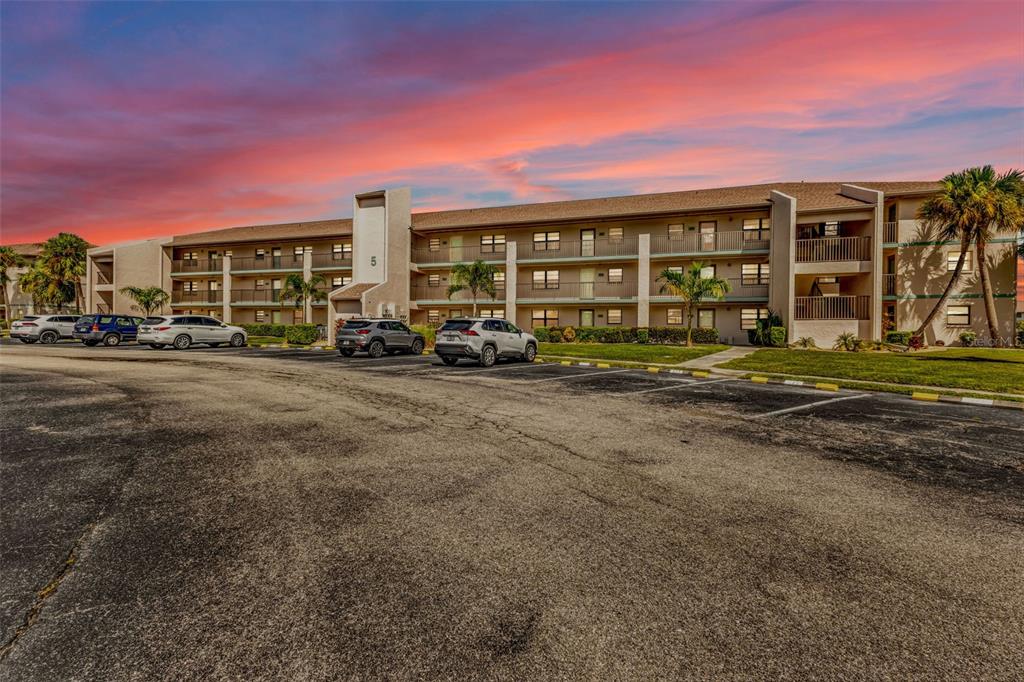 A three-story apartment building with a parking lot in the foreground under a sunset sky — 175 KINGS HIGHWAY UNIT 523, PUNTA GORDA, FL