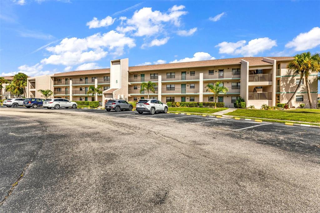 A three-story apartment building with a parking lot in the foreground under a blue sky — 175 KINGS HIGHWAY UNIT 523, PUNTA GORDA, FL