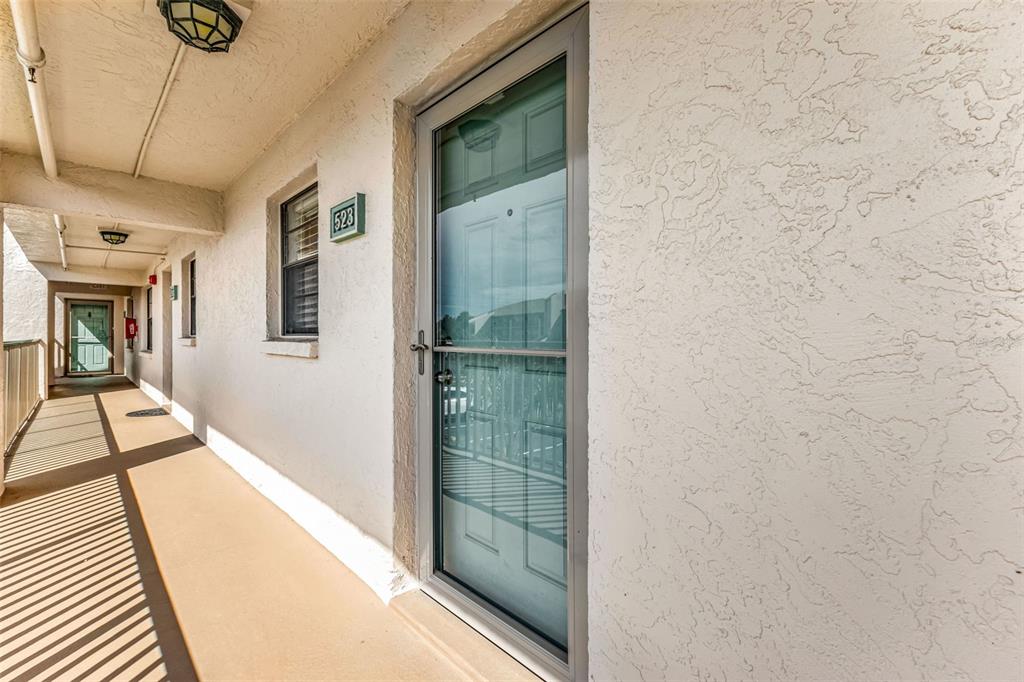 An outdoor apartment hallway with a textured wall, a screen door, and unit number 523 — 175 KINGS HIGHWAY UNIT 523, PUNTA GORDA, FL