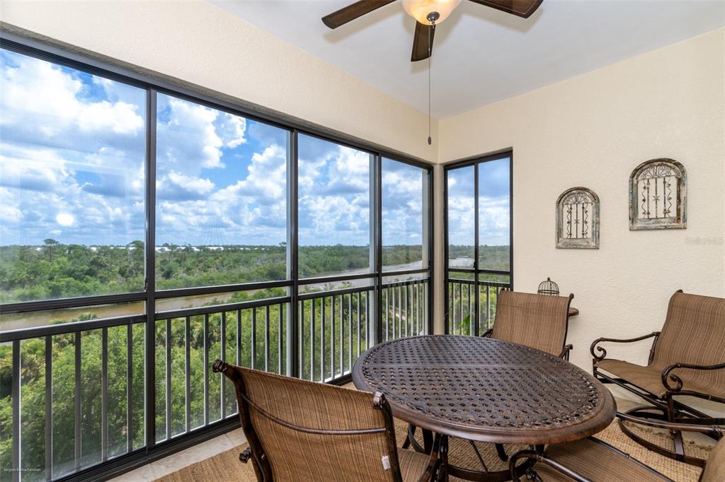 A screened-in balcony features a round table, chairs, and a view of a river — 10521 AMBERJACK WAY UNIT 303, ENGLEWOOD, FL