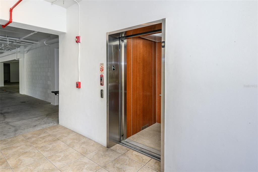 An open elevator with wood-paneled walls is located in a tiled parking garage area — 10521 AMBERJACK WAY UNIT 303, ENGLEWOOD, FL
