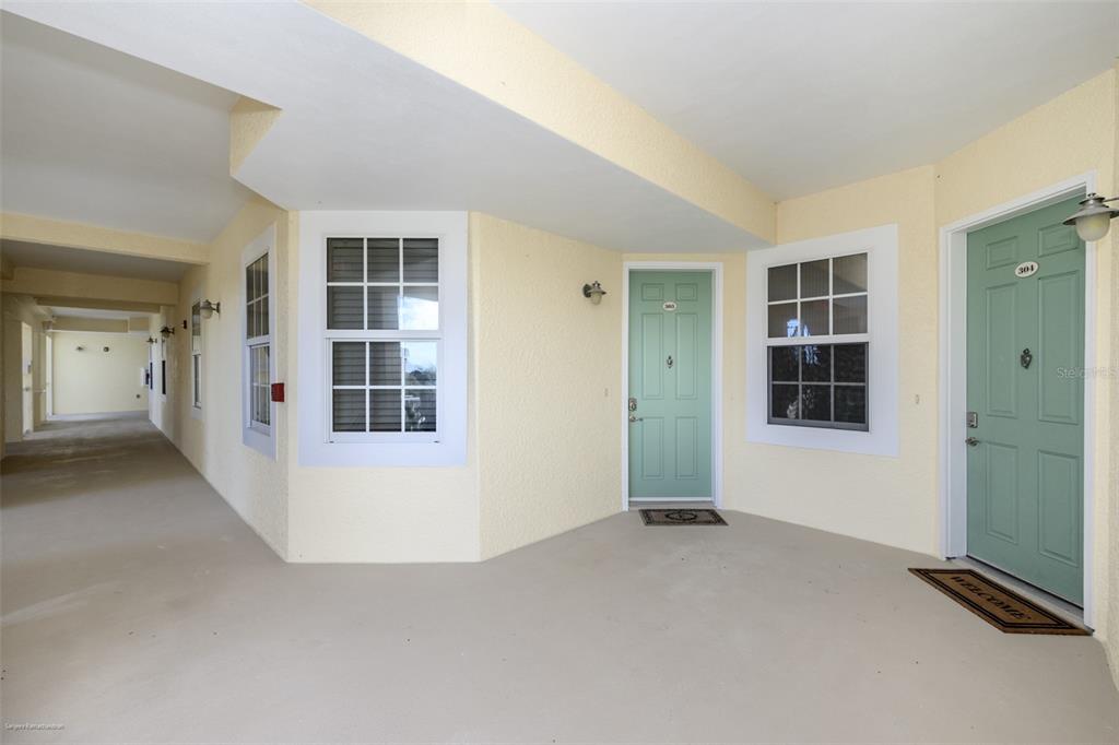 A covered outdoor walkway features two light green doors and windows against pale yellow walls — 10521 AMBERJACK WAY UNIT 303, ENGLEWOOD, FL
