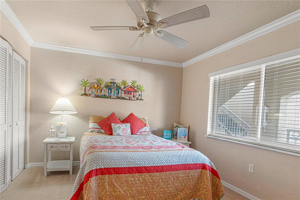 A bedroom features a bed with colorful bedding, a ceiling fan, and a wall-mounted decoration — 443 BOUCHELLE DRIVE UNIT 204, NEW SMYRNA BEACH, FL