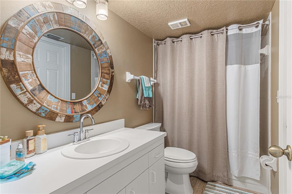 A bathroom features a white vanity, a round rustic mirror, and a shower with a curtain — 443 BOUCHELLE DRIVE UNIT 204, NEW SMYRNA BEACH, FL