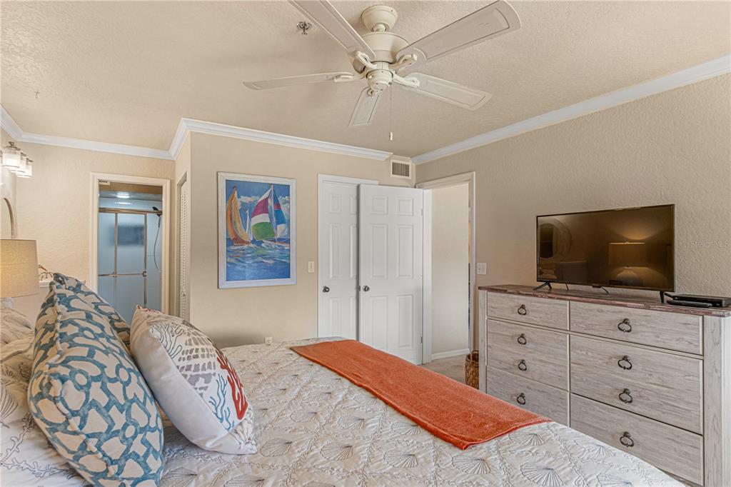 A bedroom features a bed with patterned pillows, a dresser with a television, and a ceiling fan — 443 BOUCHELLE DRIVE UNIT 204, NEW SMYRNA BEACH, FL