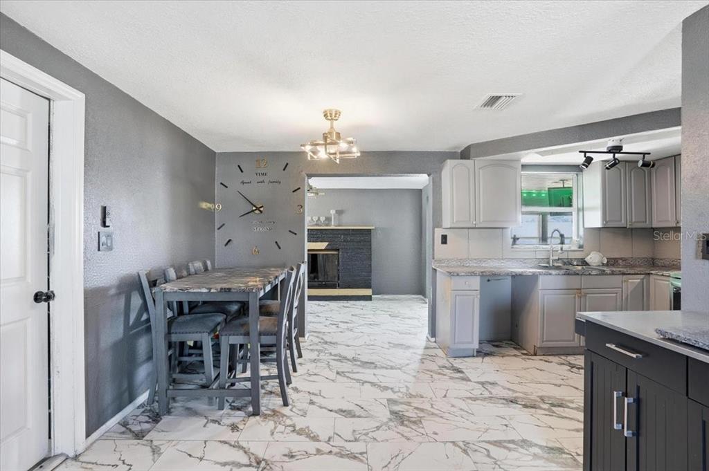 A dining area with a large wall clock opens into a kitchen with gray cabinets — 3208 KILBURN ROAD, HOLIDAY, FL