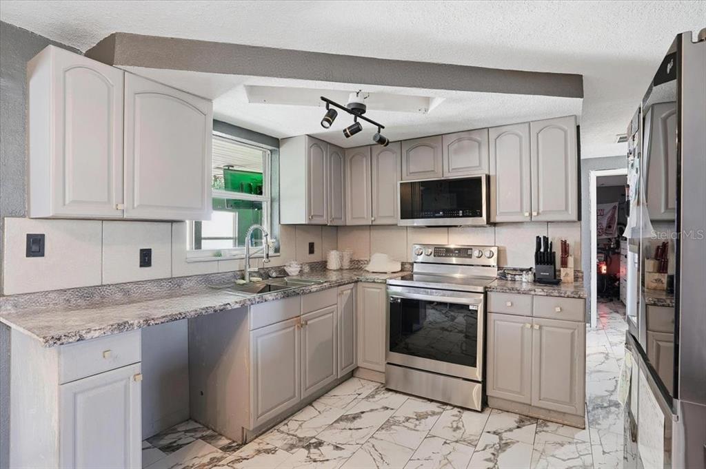 A kitchen features gray cabinets, granite countertops, stainless steel appliances, and white marble-patterned tile flooring — 3208 KILBURN ROAD, HOLIDAY, FL