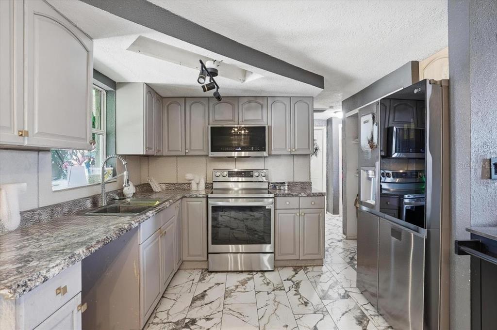 A kitchen features gray cabinets, stainless steel appliances, granite countertops, and white marble-patterned tile floors — 3208 KILBURN ROAD, HOLIDAY, FL
